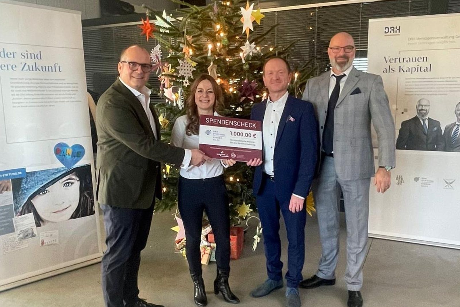 Übergabe eines Spendenschecks an die DRH Stiftung Kinderhilfe vor einem geschmückten Weihnachtsbaum